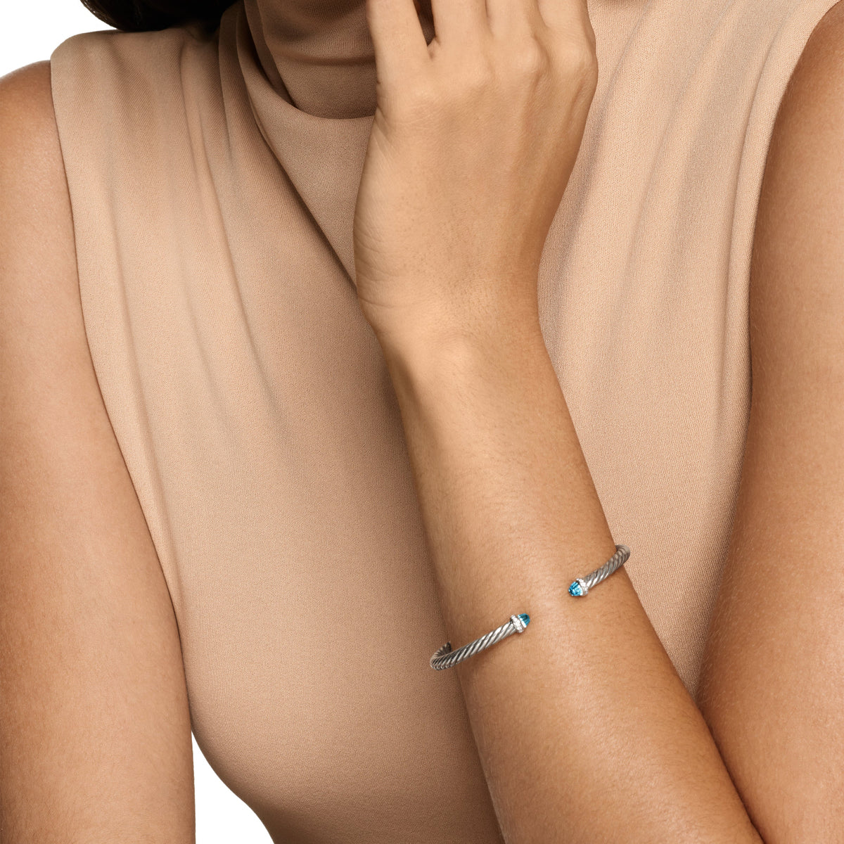 Silver bracelet with a blue gemstone on a person's wrist against a beige background